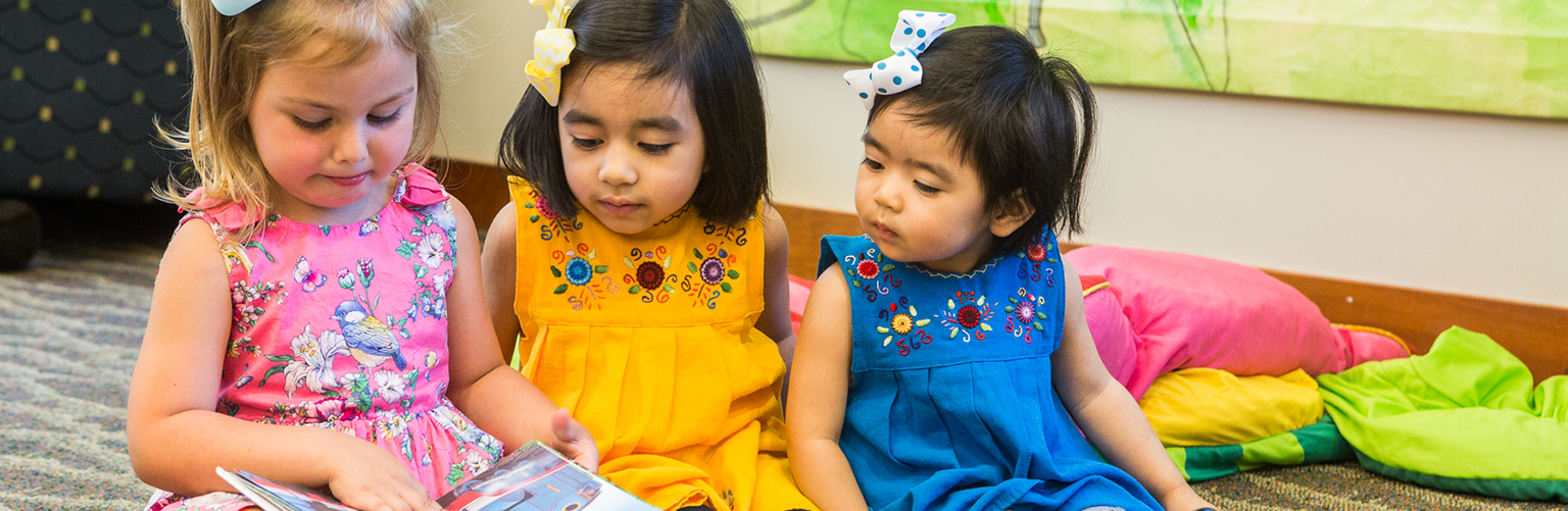 Three young girls reading from a book