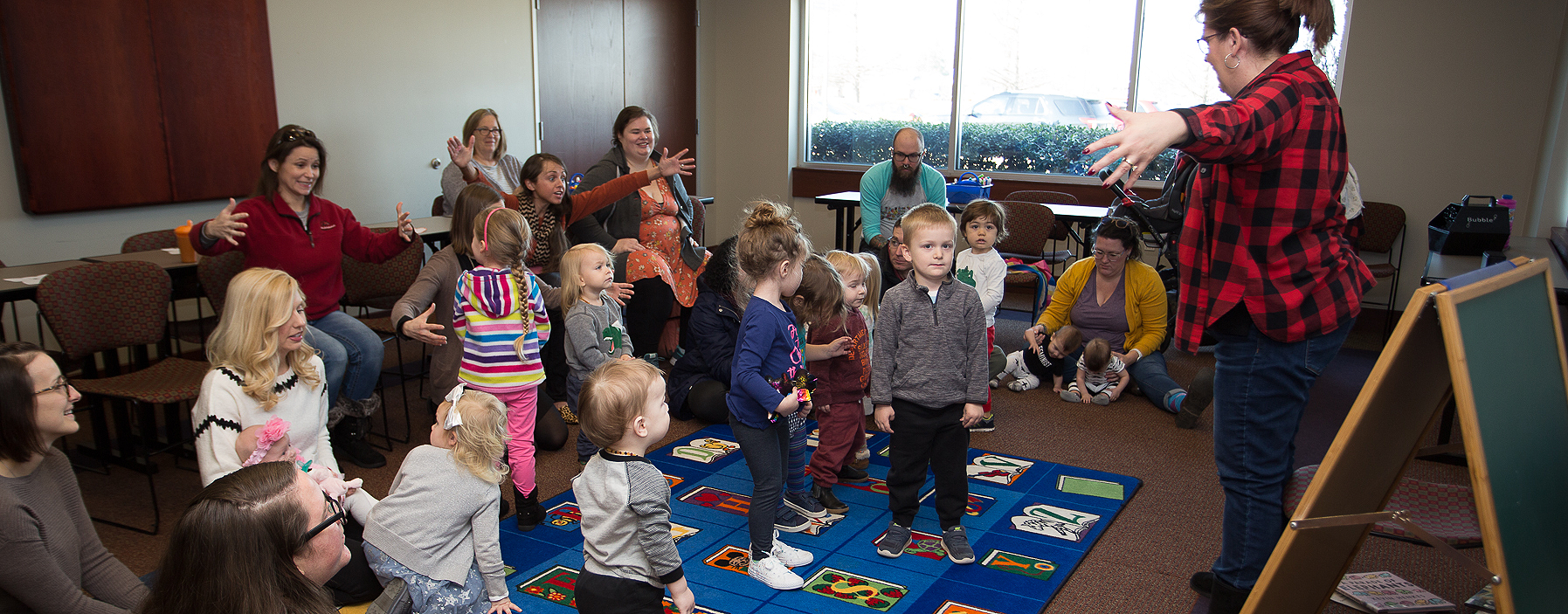 Librarian standing in front of the children with arms spread wide during storytime at Miller Branch