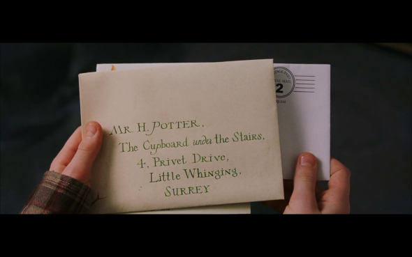 Two hands holding a envelope with the text of Mr. H Potter The Cupboard under the Stairs 4 Privet Drive, Little Whinging Surrey. 