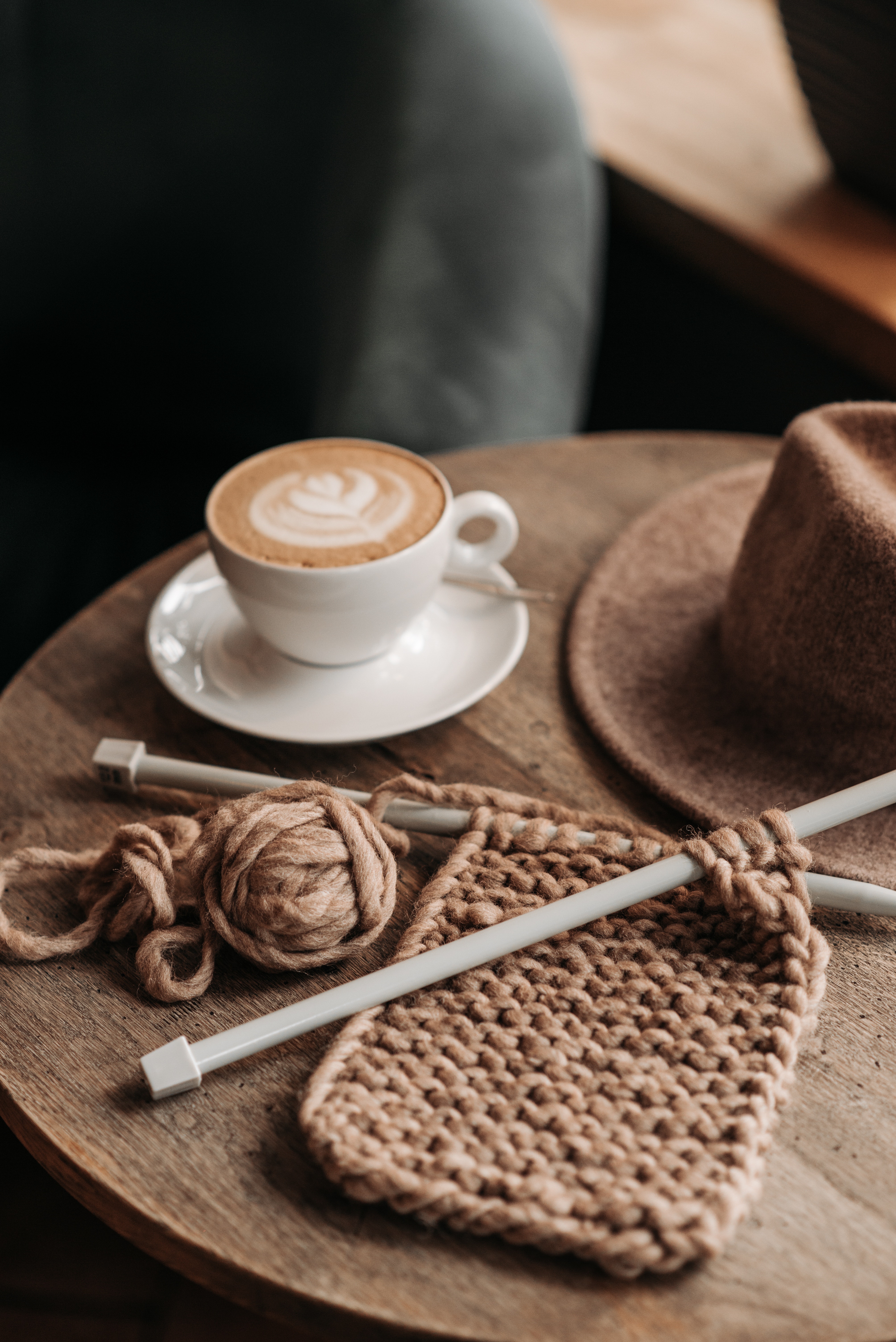 Brown crochet washcloth with needles and a coffee cup on a brown table. 