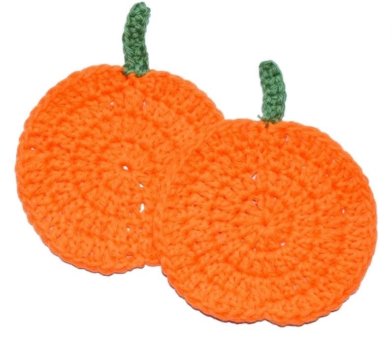 Two orange pumpkin crochet coasters with a green top against a white background. 
