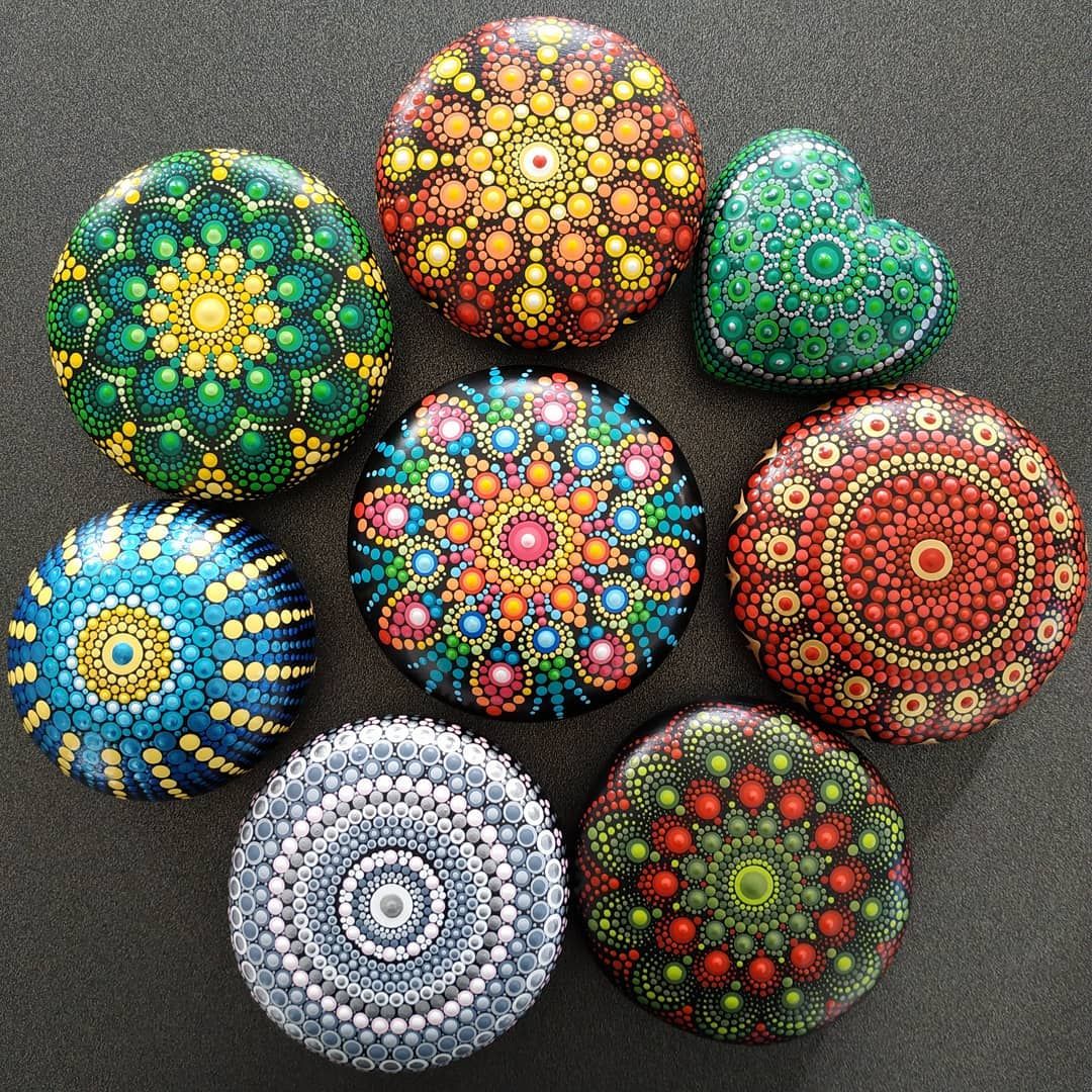 7 mandala stones covered in multiple color dots and patterns with a mandala stone in the center with same level of multicolor dots and patterns. 