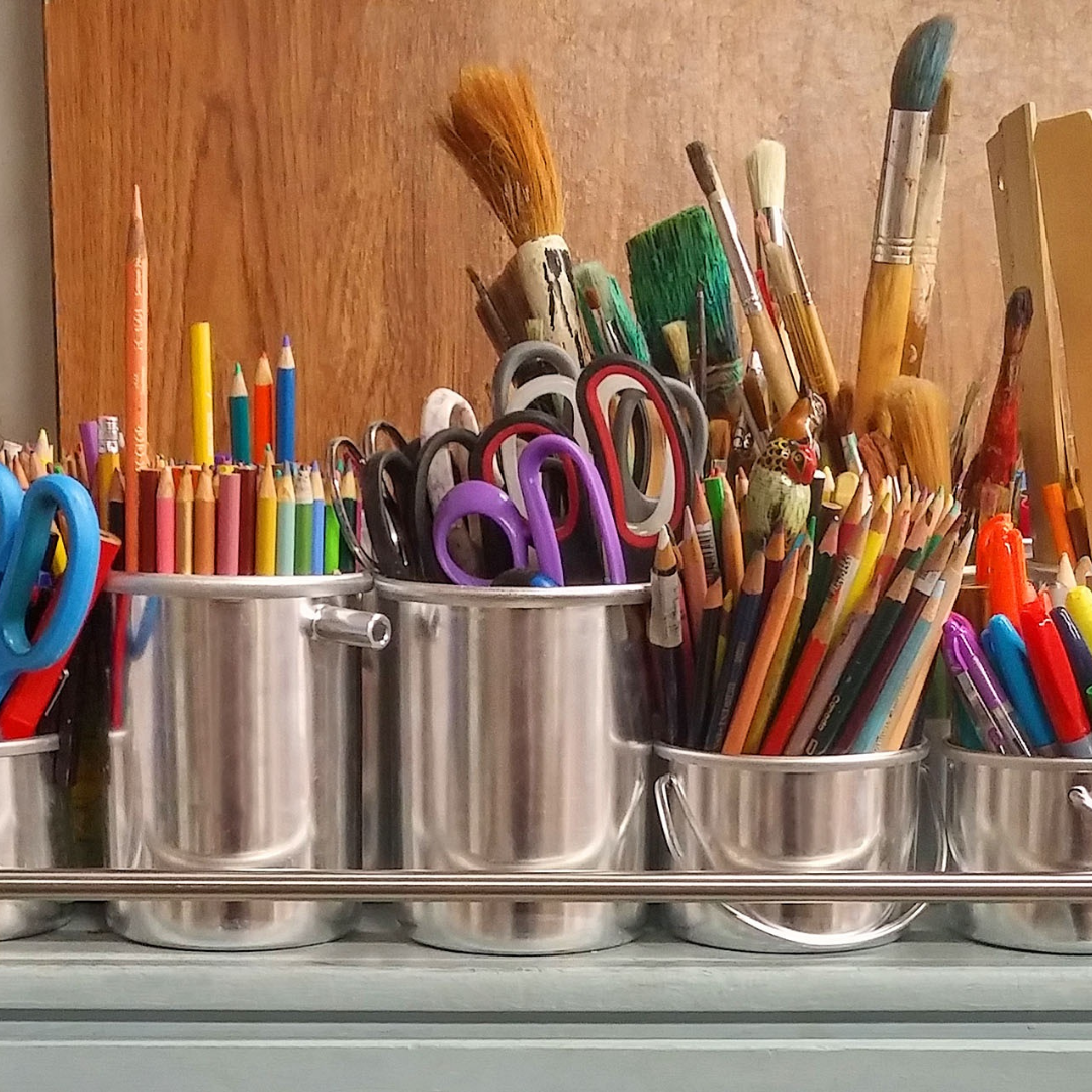 small metal buckets filled with colored pencils, scissors, and paint brushes