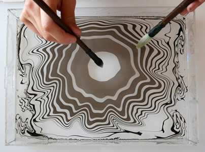 Person with a brush and two manipulating oil in water to put on a paper. 
