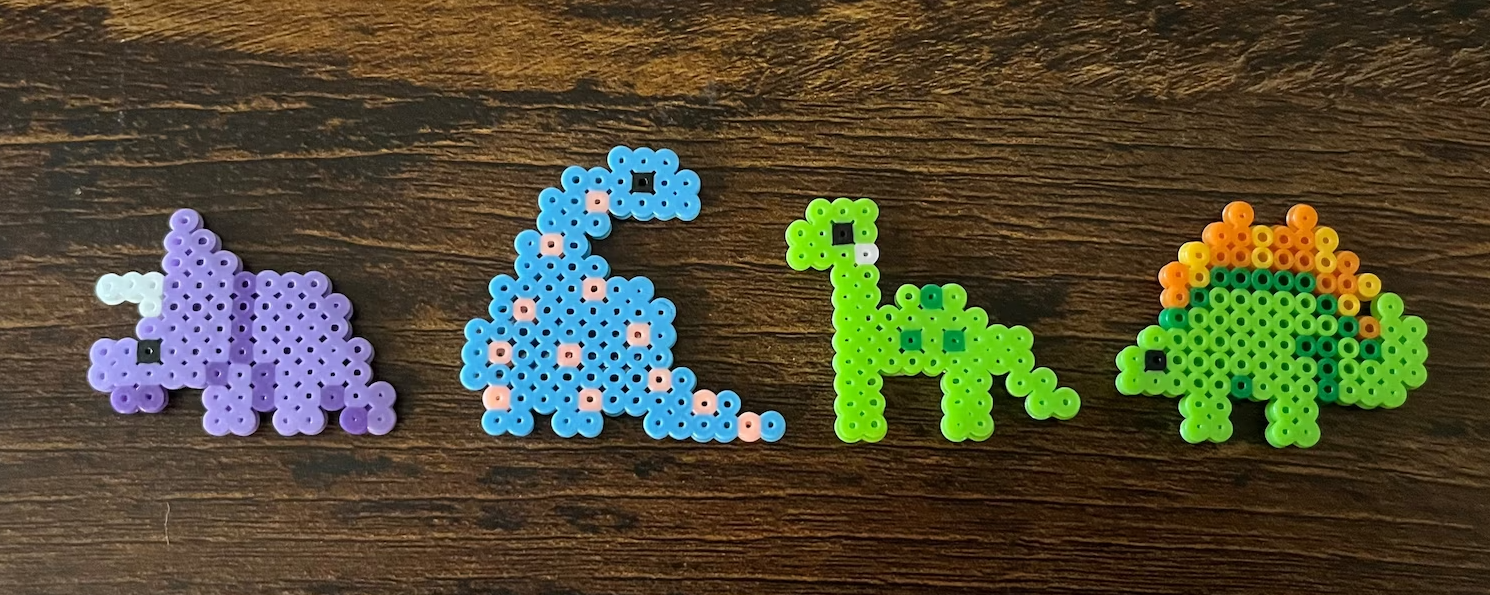 Four multicolor perler bead dinos against a wood grain background. 