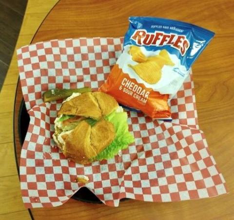 Chicken Salad Sandwich on a croissant with a bag of chips and a pickle.