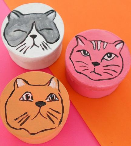 Three boxes with cats painted on the top of them in multiple colors. 