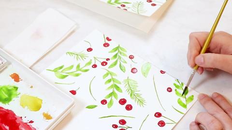 hand with paintbrush painting holly and berries
