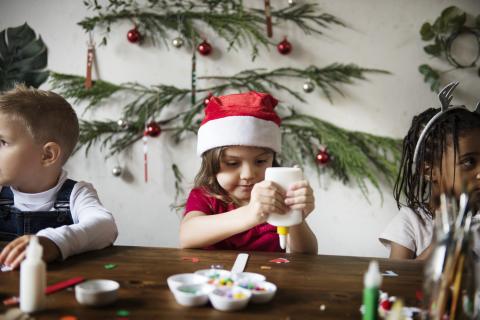 little girl in Santa hat with a glue bottle making a craft