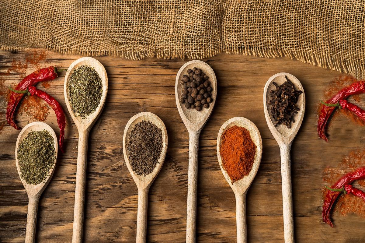 Different colored spices in wooden spoons on a woodish color background.