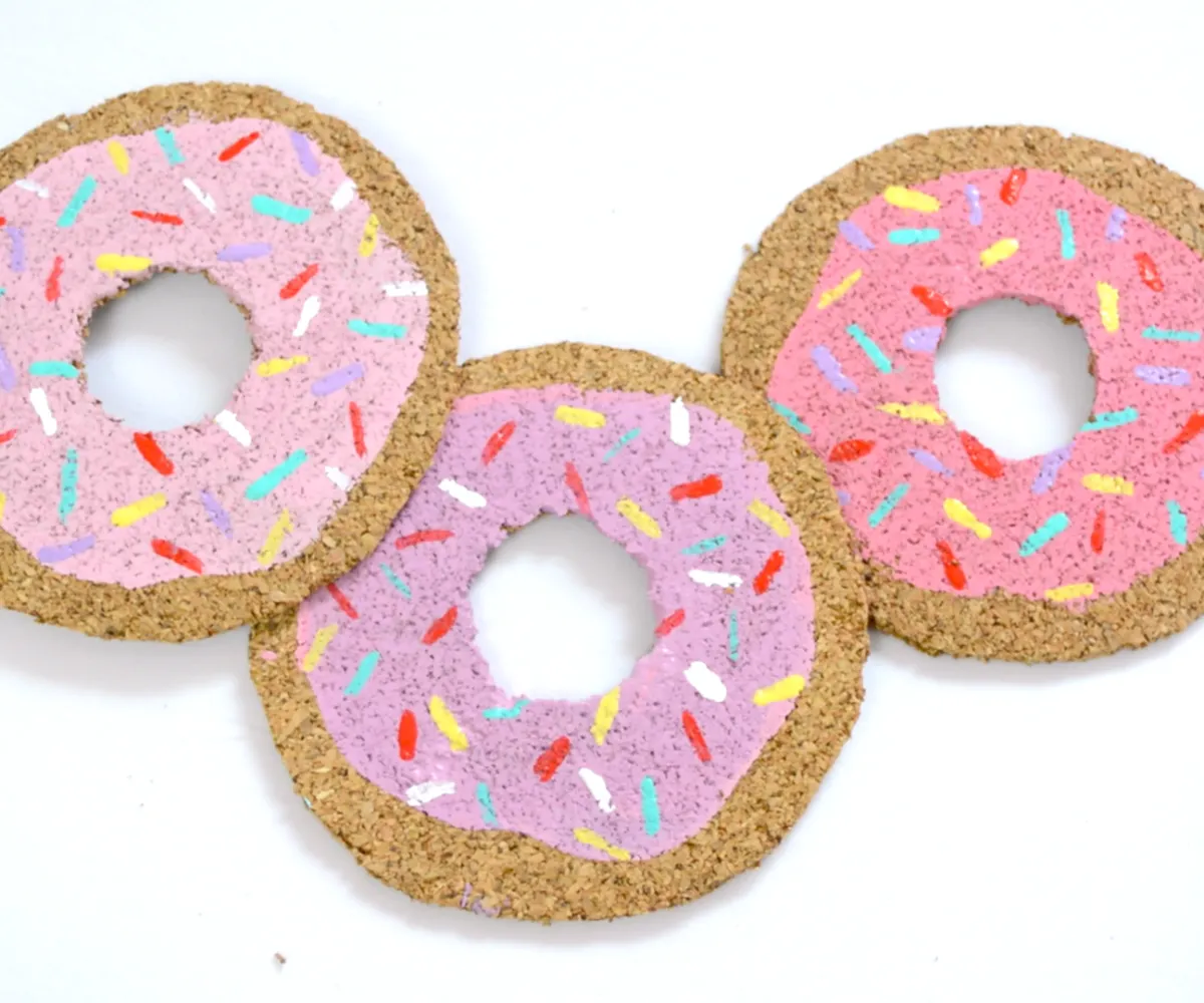 Three cork donut coasters with pink frosting and sprinkles on top. 