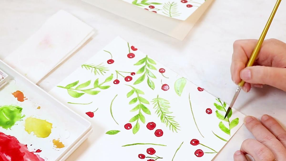 hand with paintbrush painting holly and berries